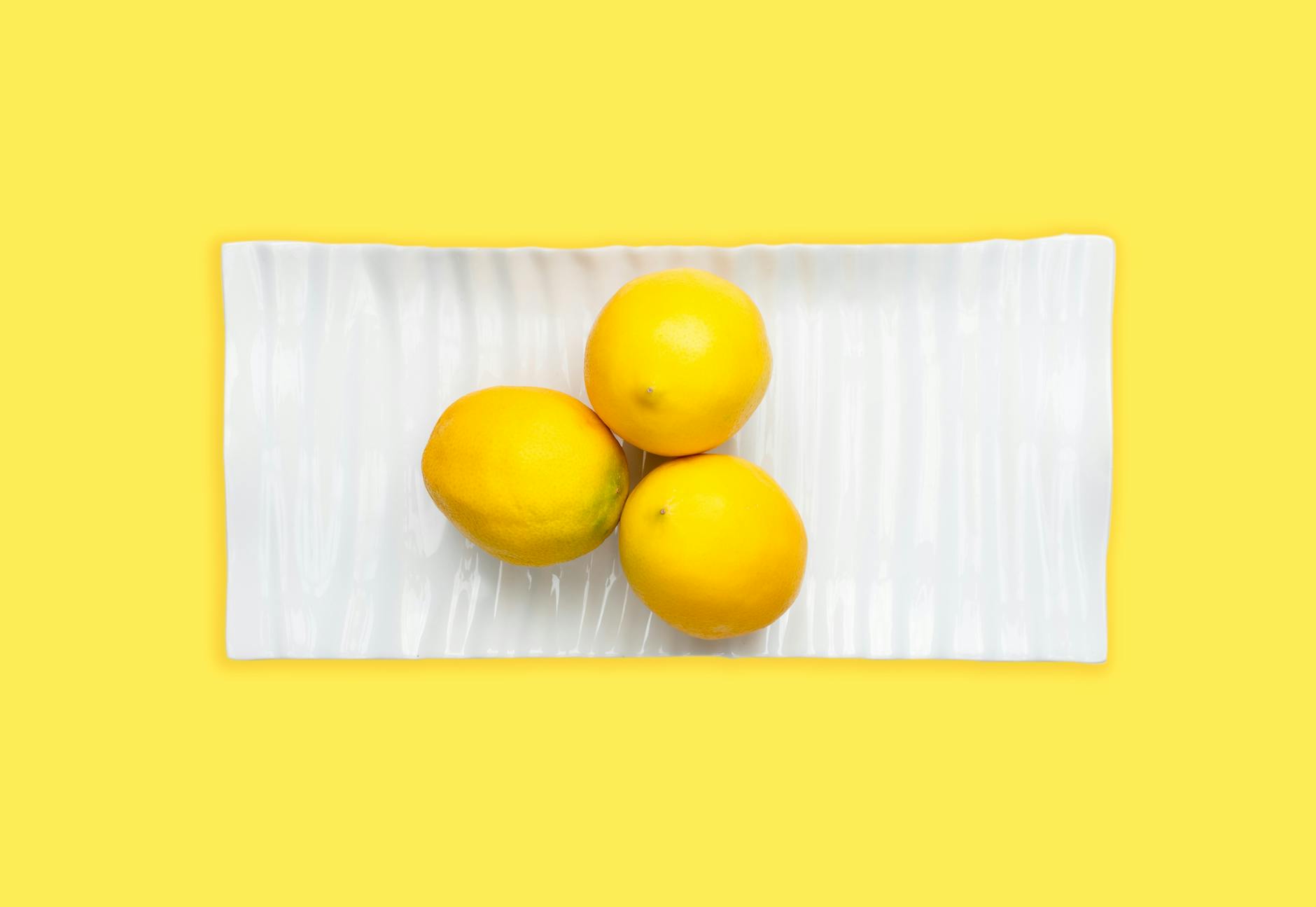 Tres limones frescos en un plato blanco sobre un fondo amarillo vibrante, representando la vitalidad y la frescura