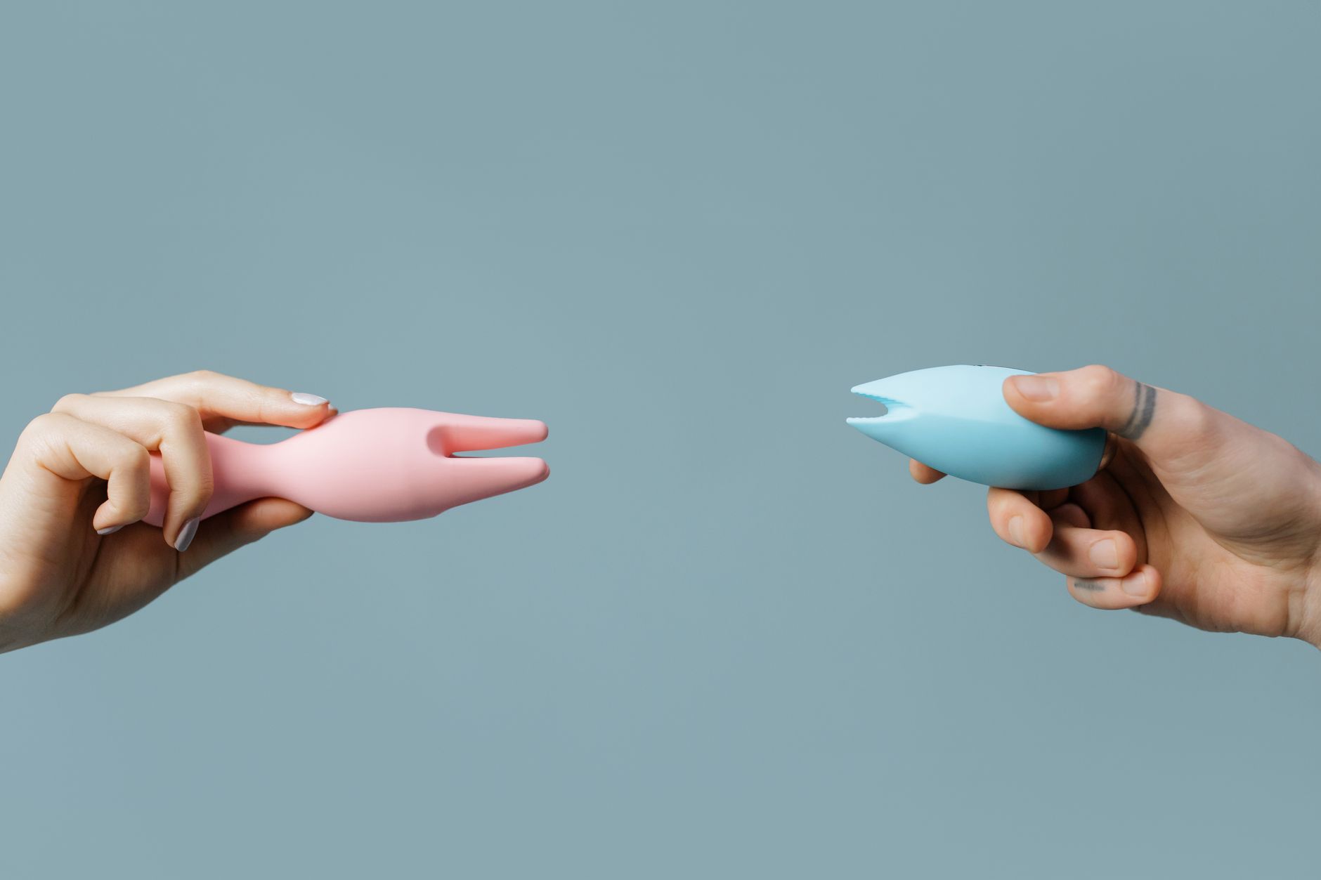 Two silicone vibrators held in hands against a pastel background.