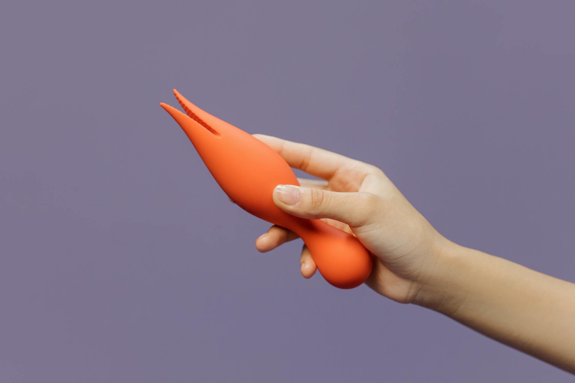 A close-up of a hand holding a vibrator against a minimalistic purple backdrop, showcasing modern sensuality and connection