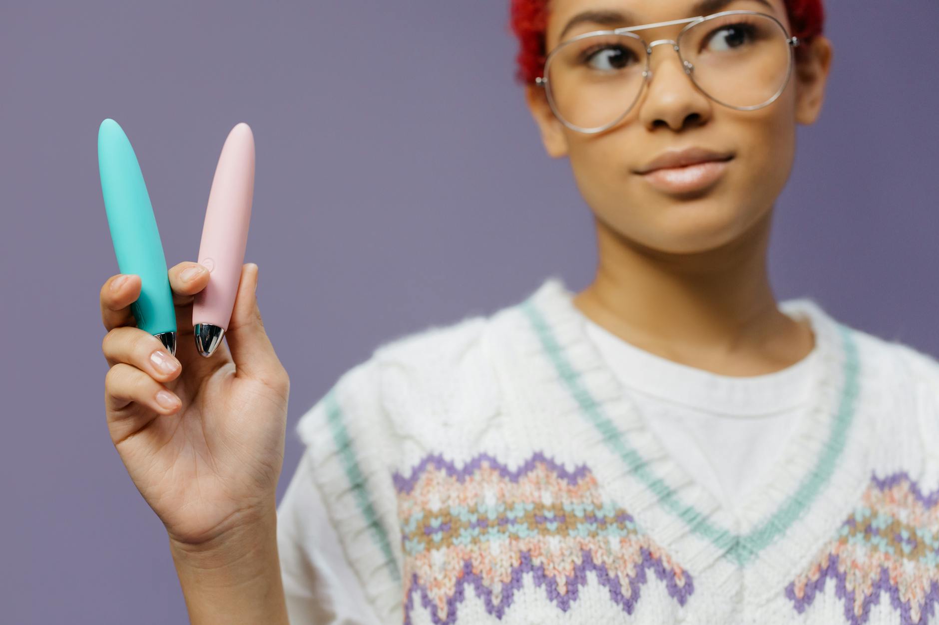 Mano sostiene un vibrador de silicona azul contra un fondo púrpura sólido, promoviendo el amor propio y la sexualidad