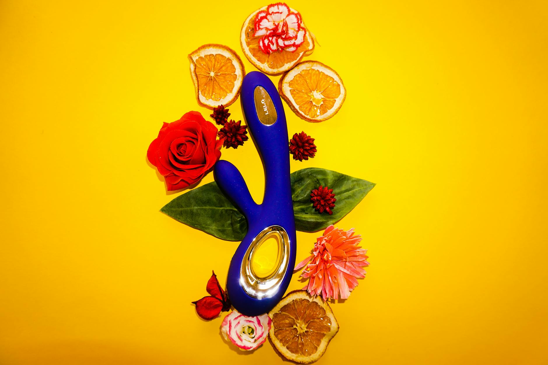 A blue clitoral vibrator surrounded by fresh lemons and citrus slices on a bright yellow background